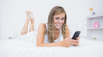 Happy woman lying on the bed with her phone