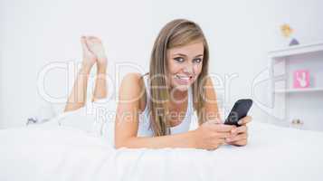 Happy woman lying on the bed with her phone