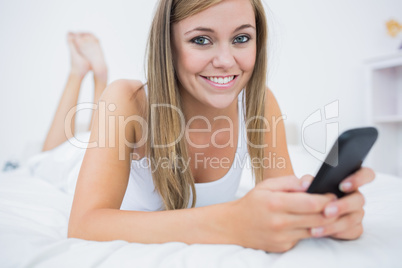 Cute woman lying on the bed with her phone