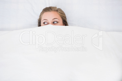 Blonde woman hiding under the duvet