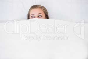 Blonde woman hiding under the duvet