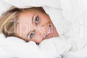 Smiling woman hiding under the duvet