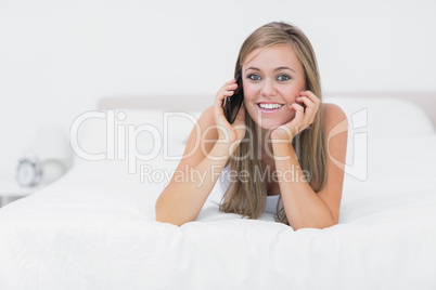 Cheerful woman phoning lying on the bed