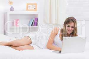 Blonde woman lying on her bed with a laptop