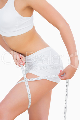 Slim woman measuring thigh with tape measure