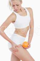 Woman checking out fat on thigh as she holds orange
