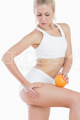 Attractive woman checking out fat on thigh as she holds orange