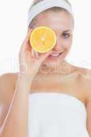 Happy woman holding orange slice in front of eye