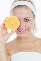 Happy woman holding slice of orange in front of eye