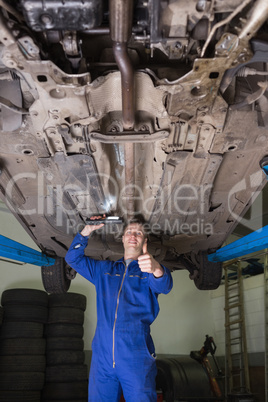 Male mechanic under car gesturing thumbs up