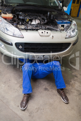 Male mechanic lying under car