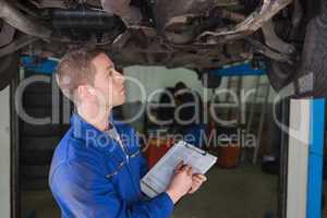 Mechanic under car preparing checklist