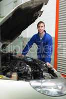 Happy mechanic standing by car