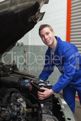 Happy mechanic with battery by car