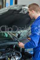 Mechanic with tablet pc examining car engine