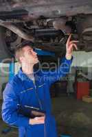 Auto mechanic with clipboard under car