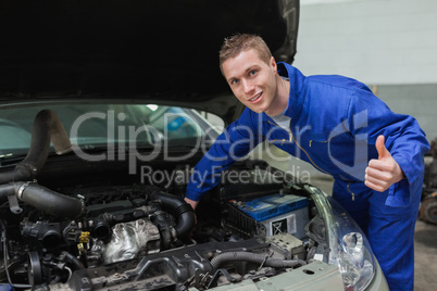 Mechanic under car bonnet gesturing thumbs up