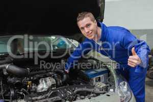 Mechanic under car bonnet gesturing thumbs up