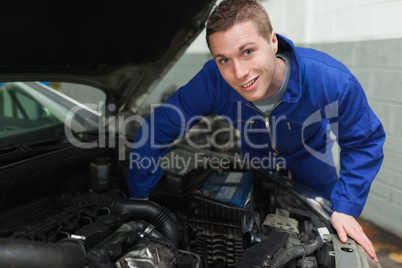 Happy mechanic repairing under car hood
