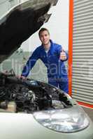 Auto mechanic by car gesturing thumbs up