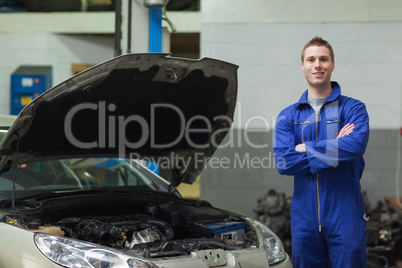 Confident mechanic standing by car