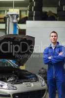 Happy mechanic standing by car with open hood