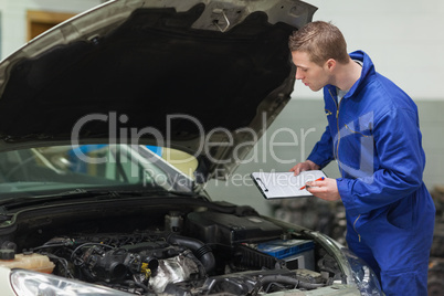 Mechanic with clipboard examining car engine