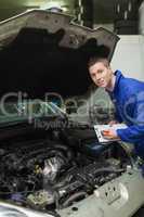 Auto mechanic with clipboard examining car