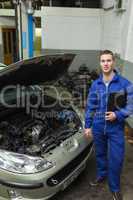 Confident mechanic standing by car with open hood