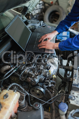 Mechanic hands using laptop on car engine