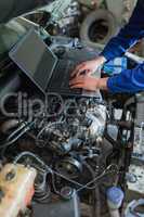 Mechanic hands using laptop on car engine