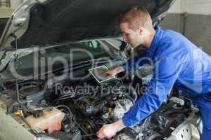 Mechanic with digital tablet repairing car engine