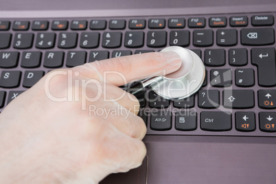 Hand examining laptop keyboard with stethoscope