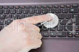 Hand examining laptop keyboard with stethoscope