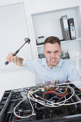 Portrait of frustrated man hitting cpu with hammer