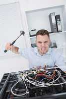 Portrait of frustrated man hitting cpu with hammer