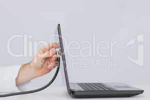 Hand examining laptop with stethoscope