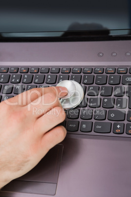 Hand examining laptop keyboard with stethoscope