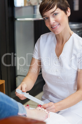 Portrait of nail technician filing woman's toe nails