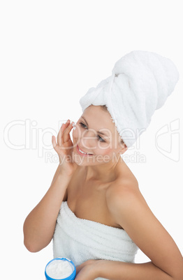 Happy woman wrapped in towel applying cream on face