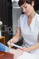 Nail technician filing woman's toe nails at nail salon