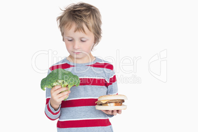 Young boy holding broccoli and burger