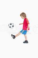 Side view of little boy kicking football
