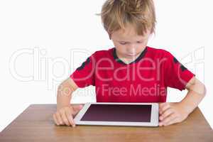 Little boy sitting at desk and looking at digital tablet