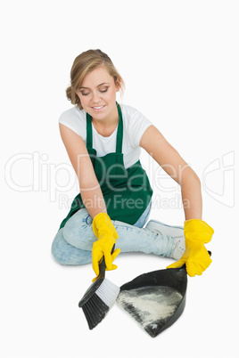 Smiling young maid using brush and dust pan