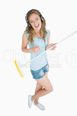 Woman playing air guitar with broom while listening music over h