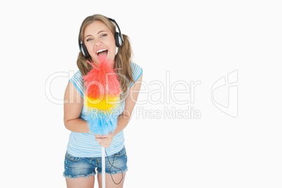 Woman holding feather duster as microphone and listening music o