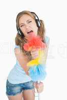 Woman holding feather duster as microphone and listening music o