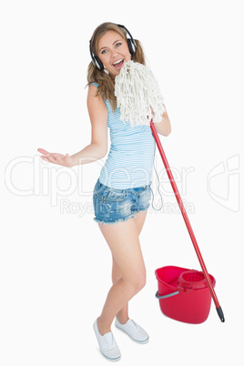 Woman holding broom as microphone and listening music over headp