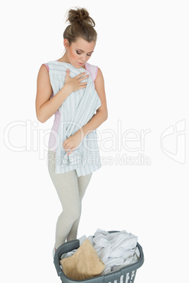 Young woman folding shirt with laundry basket